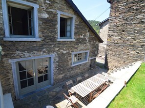 A stone building with a patio area featuring a wooden table and chairs. - Cozy Cottage Near River (Vresse-sur-Semois)