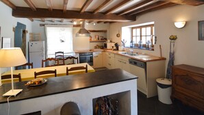 A rustic kitchen with exposed wooden beams, a central island, and a window overlooking a garden. - Cozy Cottage Near River (Vresse-sur-Semois)