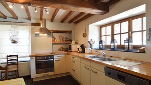 A kitchen with wooden beams, a stove, oven, sink, and a window with a view. - Cozy Cottage Near River (Vresse-sur-Semois)