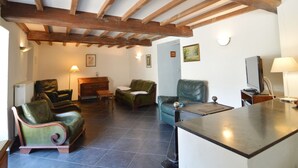 A living room with a high ceiling, wooden beams, a fireplace, and a television. - Cozy Cottage Near River (Vresse-sur-Semois)