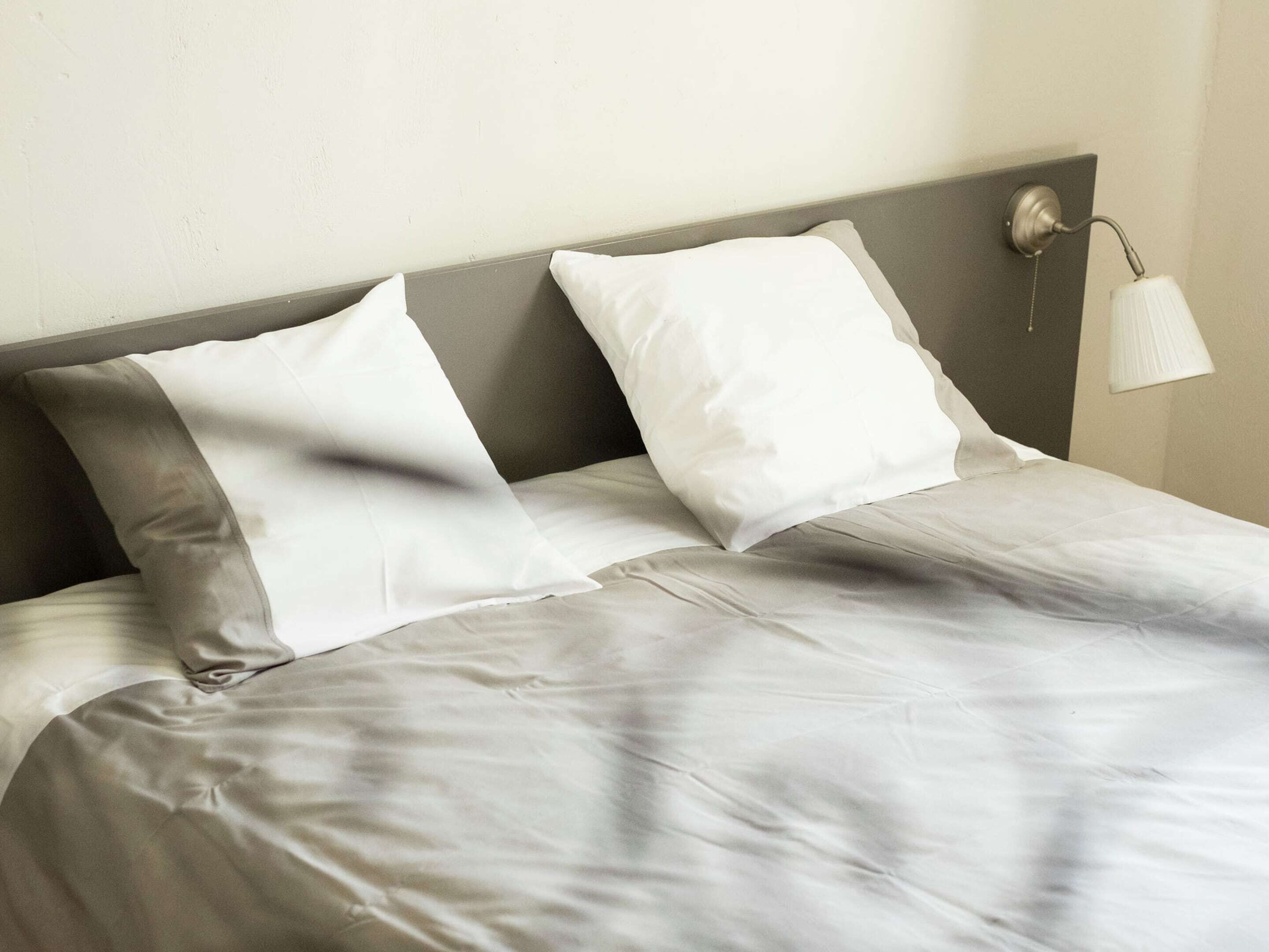 Una cama bien hecha con cabecera gris y dos almohadas blancas.