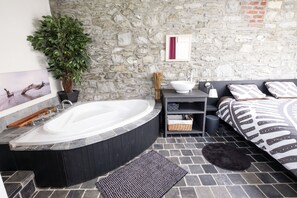 A bathroom with a stone wall, a bathtub, a sink, a mirror, and a potted plant.