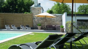 Una zona junto a la piscina con sillones de descanso, un muro de piedra y una chimenea.