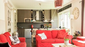 Una sala de estar moderna con sofás rojos y una mesa de centro de madera, una cocina con armarios oscuros y electrodomésticos blancos, y un gran ventanal que proporciona luz natural.