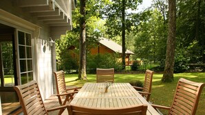 Una terraza de madera con una mesa y seis sillas, rodeada de un jardín exuberante y árboles.