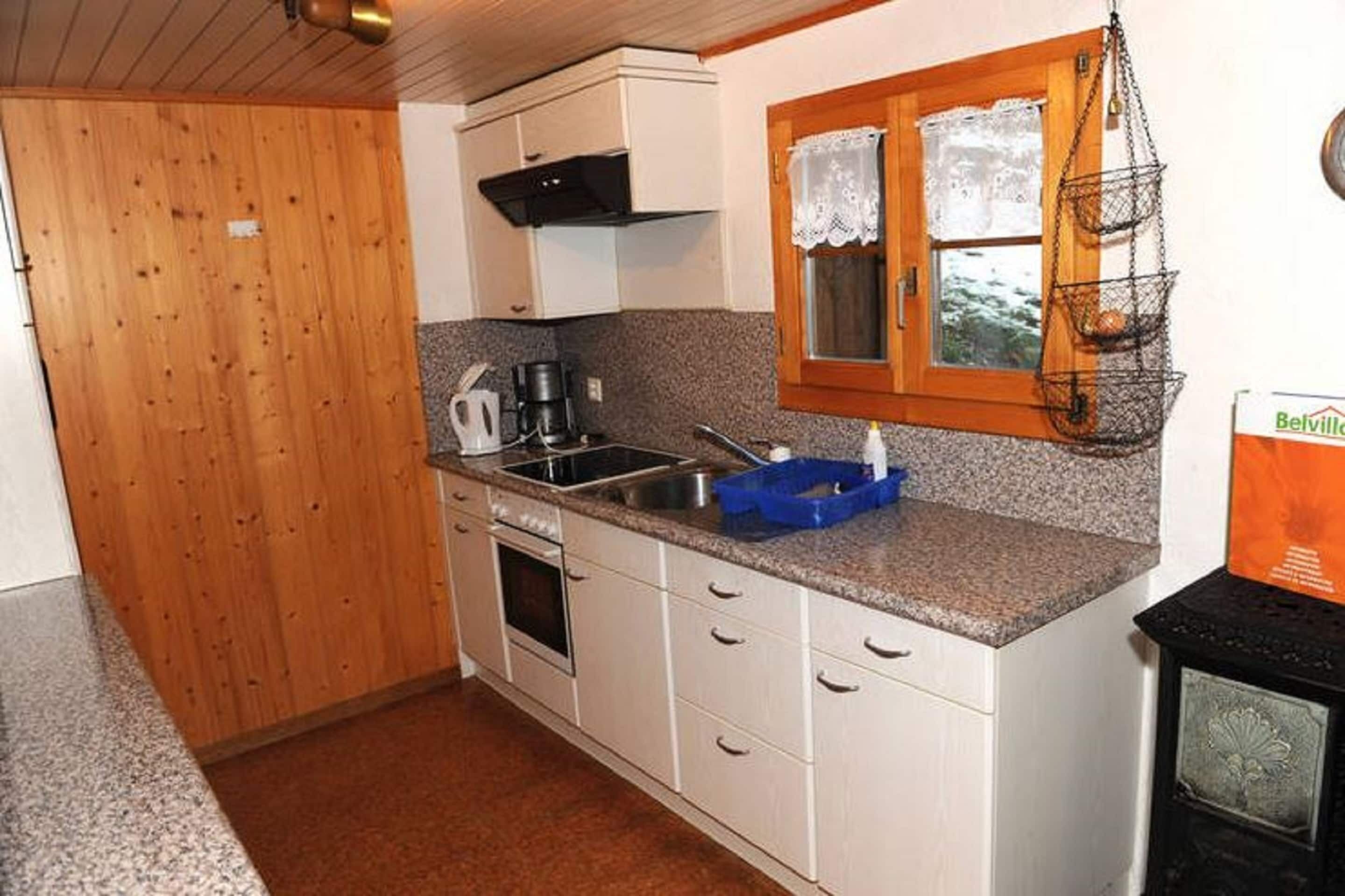 A compact kitchen with white cabinets, a granite countertop, a stove, and a hanging fruit basket.