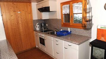 A compact kitchen with white cabinets, a granite countertop, a stove, and a hanging fruit basket.