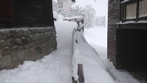 Un sendero cubierto de nieve que conduce a un edificio de piedra con una valla de madera.