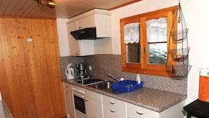 Una cocina compacta con armarios blancos, encimera de granito, estufa y una cesta colgante.