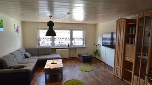 Uma sala de estar com sofá seccional, uma mesinha, televisão e um armário.