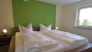 Uma cama de casal com roupa de cama branca, uma cabeceira de madeira e duas luminárias de apoio.