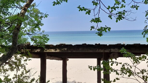 A beach view with a wooden structure and trees in the foreground. - Modernes Ferienhaus mit Sauna in Wiek am Meer (Wiek)