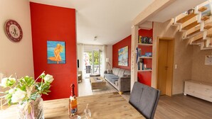 A modern living room with a wooden dining table, a sofa, and a staircase. - Modernes Ferienhaus mit Sauna in Wiek am Meer (Wiek)