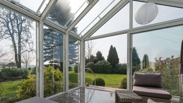 A conservatory with a glass roof, offering a view of a well-maintained garden and trees. - Spacious Apartment in Leopoldshöhe near Teutoburg Forest (Leopoldshoehe)