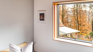 A room with a large window, a framed picture on the wall, and a wooden ceiling.
