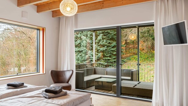 A modern bedroom with a large bed, a chair, and a balcony with outdoor seating.