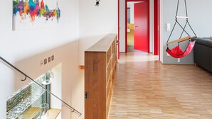 A modern interior with a wooden staircase, a red hanging chair, and a colorful cityscape painting.