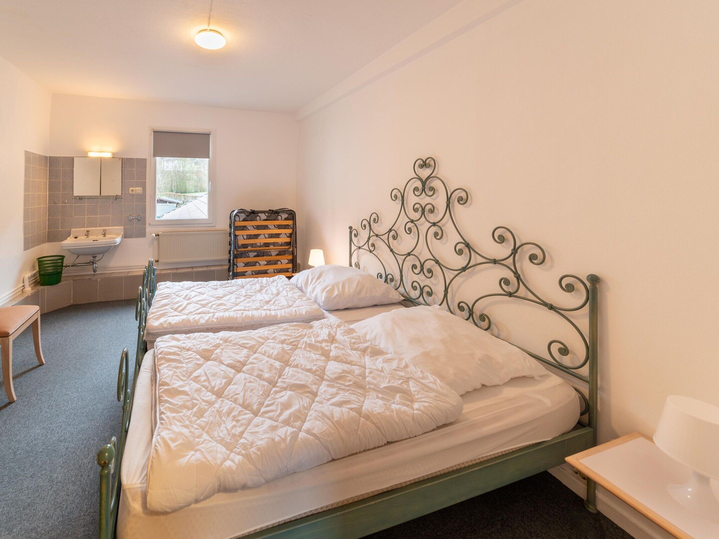 Une chambre avec deux lits, un lavabo, un miroir et une fenêtre.