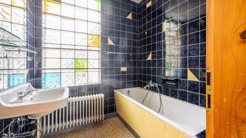 Un baño con bañera, lavamanos y una ventana con vidrieras.