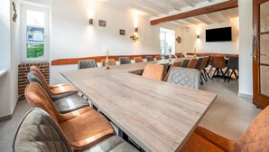 A conference room with a long table and multiple chairs, white walls, and ceiling beams.