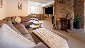 A cozy living room with a brick fireplace, a large flat-screen TV, a sofa, and a coffee table.