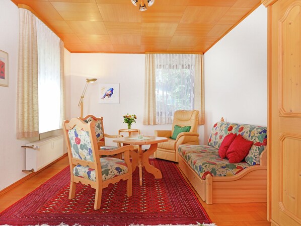A cozy room with a wooden ceiling, a wooden sofa with floral upholstery, a wooden dining table with chairs, and a red patterned rug. - Holiday in the Sauerland Region in Unique Location (Willingen)