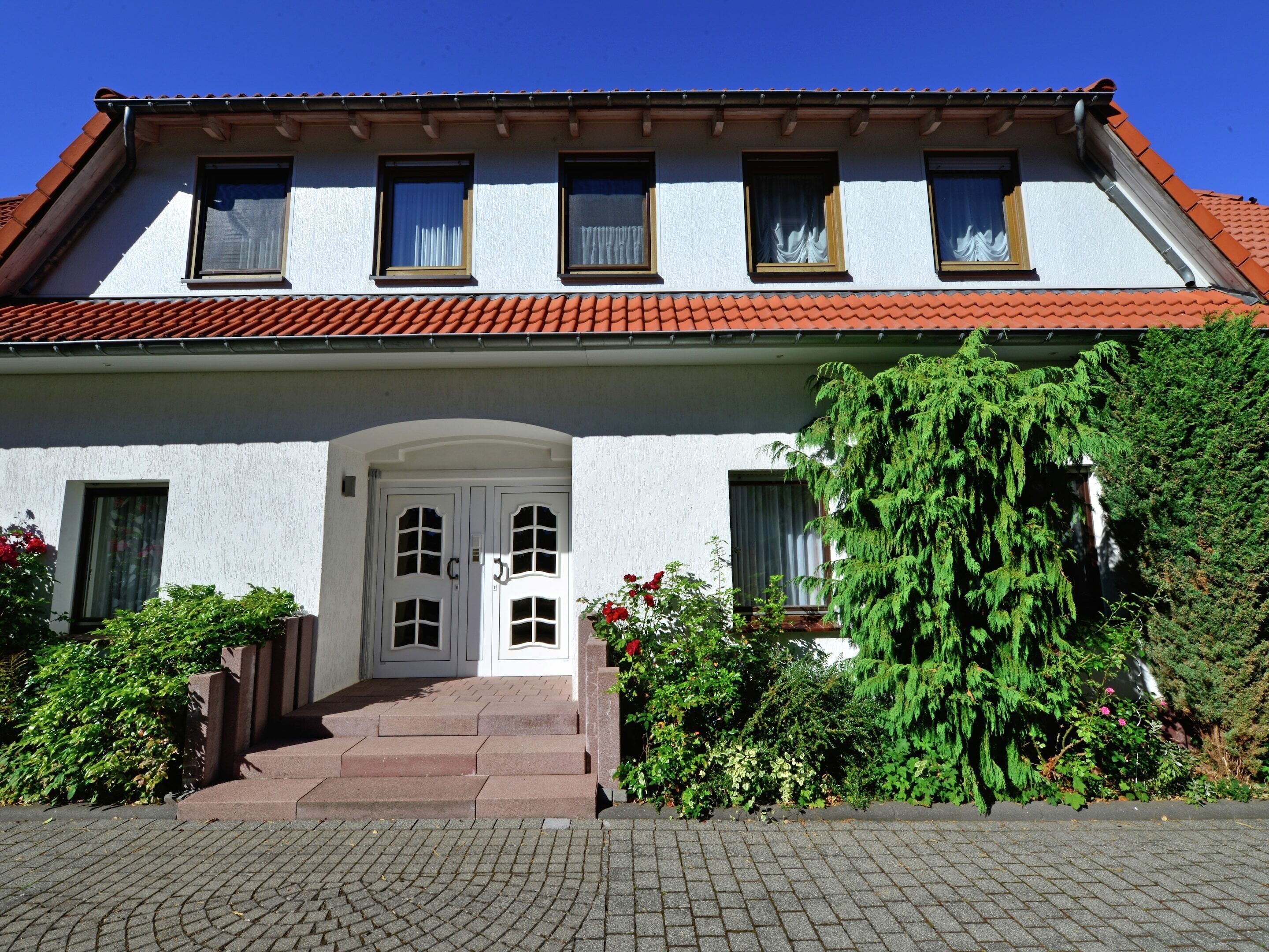 A two-story building with a red-tiled roof, white exterior walls, and a central entrance with a door and steps.