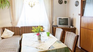 Un salon chaleureux avec un canapé, une table à manger recouverte d’une courtepointe, un téléviseur et une plante.