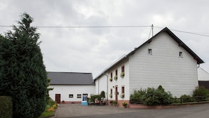 Un bâtiment à deux étages, doté d’un toit recouvert de tuiles, d’un porche à l’avant avec des chaises et d’un petit jardin.