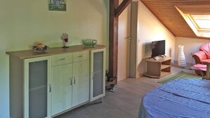 A room with a wooden ceiling, a bed with a blue cover, a television, a pink chair, and a cabinet with glass doors.