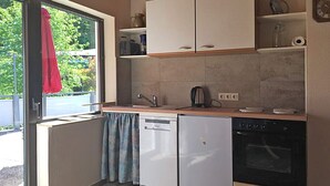 A compact kitchen with a dishwasher, oven, and a window with a red towel hanging.