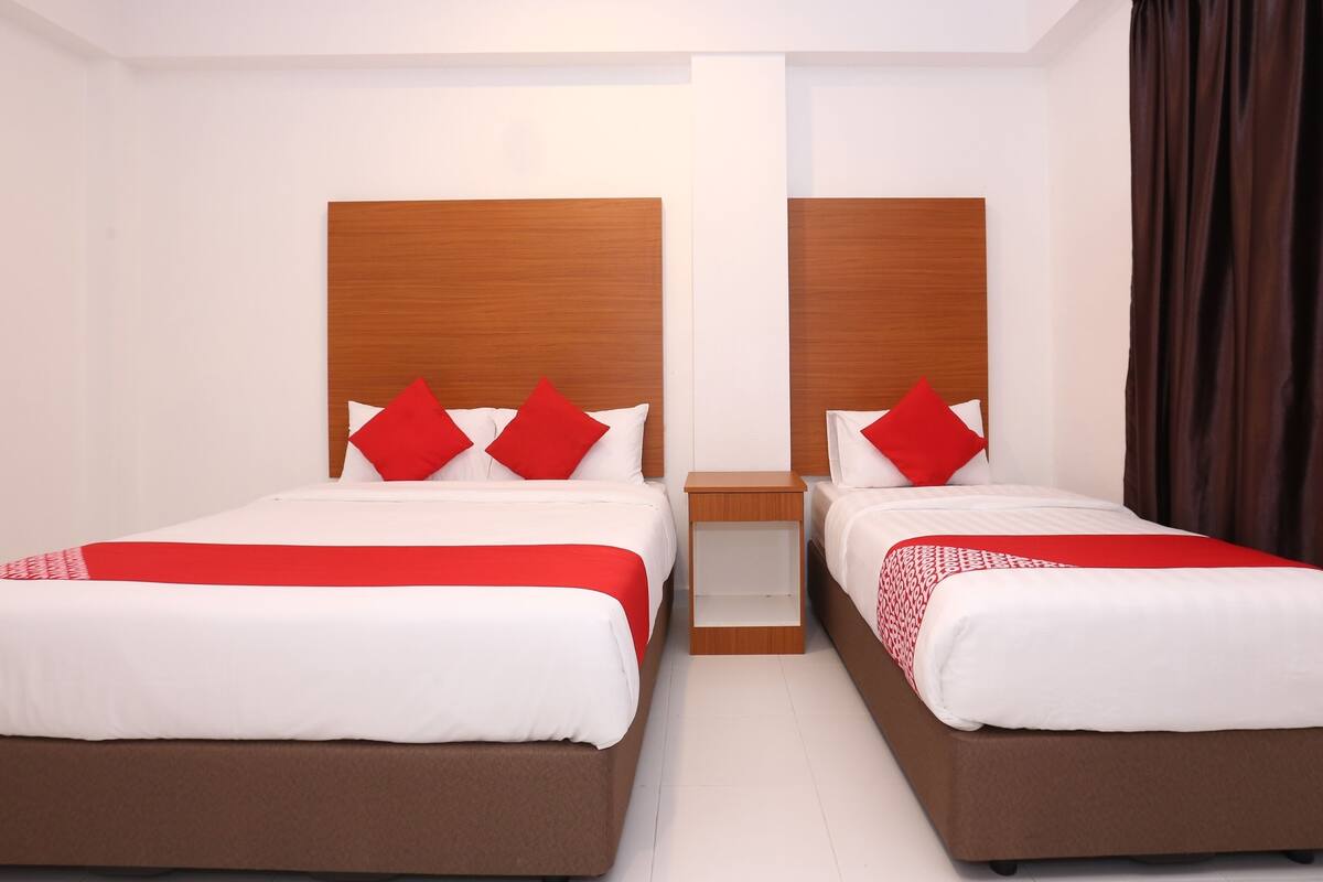 A hotel room with two beds, each with a wooden headboard, white bedding, and red pillows.