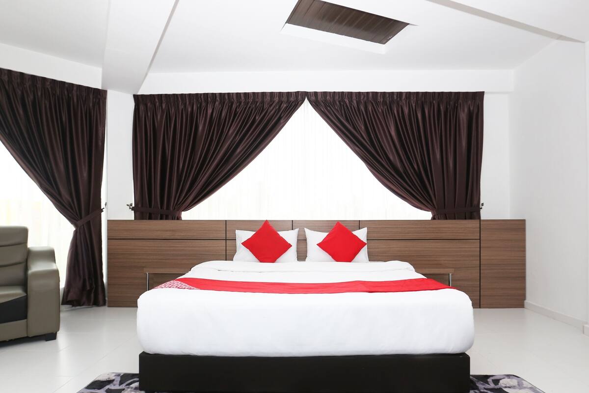 A modern bedroom with a large bed, dark curtains, and a patterned rug.
