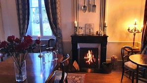A cozy room with a fireplace, a dining table with chairs, and a vase of red roses. - Beautiful Manor house with heated pool in a village,  close to sandy beaches. (EPARGNES)
