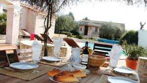 A dining table set outdoors with plates, glasses, and a bottle, surrounded by lounge chairs and a pool in the background. - Villa in Languedoc With Pool Near Historic Cities (Rousson)