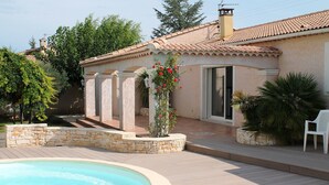 A swimming pool with a stone border, a patio area, and a building with a tiled roof. - Villa in Languedoc With Pool Near Historic Cities (Rousson)