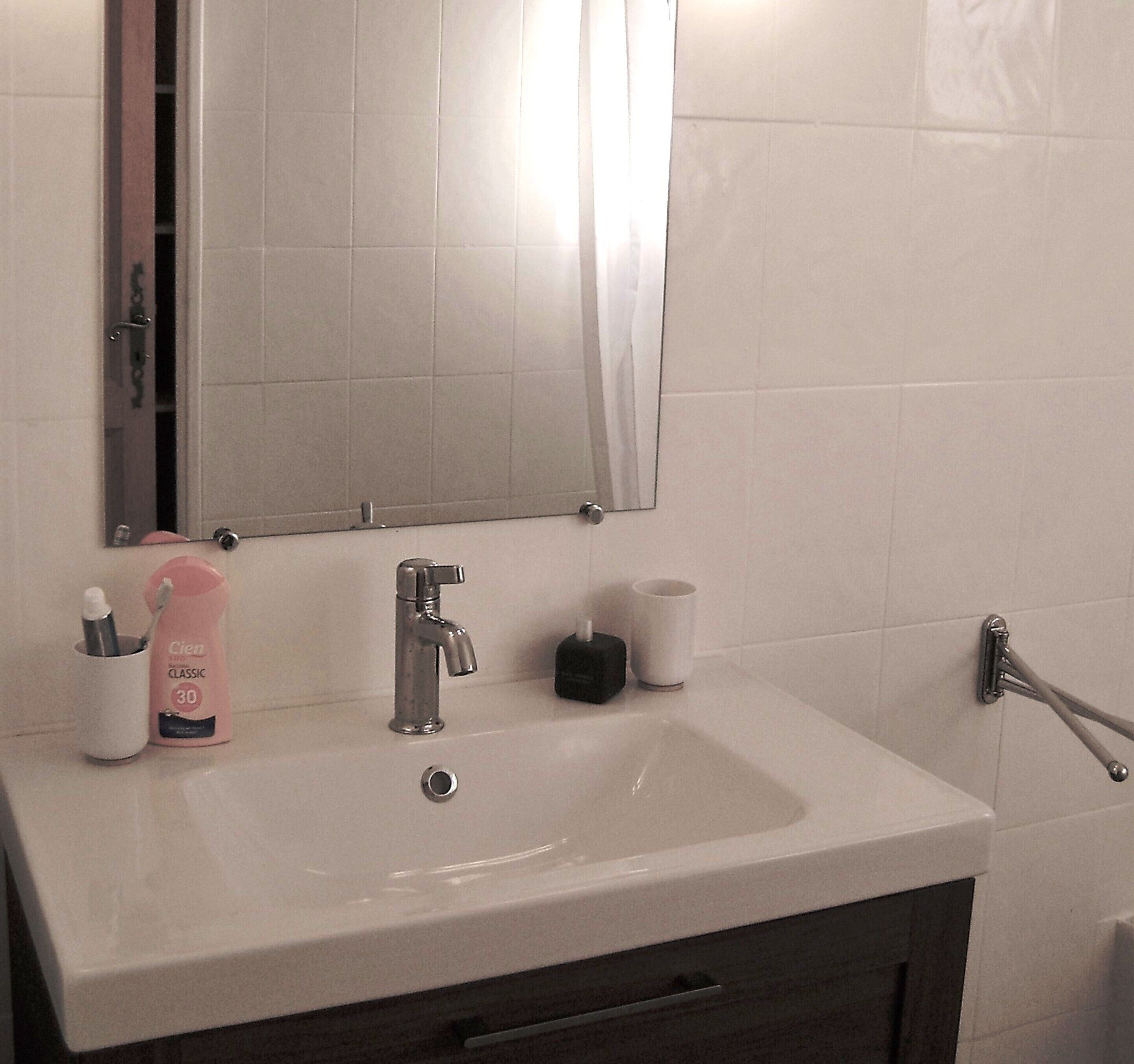 Ein Badezimmer mit einem weißen Waschbecken, einem Spiegel, einer Zahnbürstenhalterung und einer Tasse.