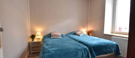 A bedroom with two beds, bedside tables with lamps, a window with a view, and a radiator.
