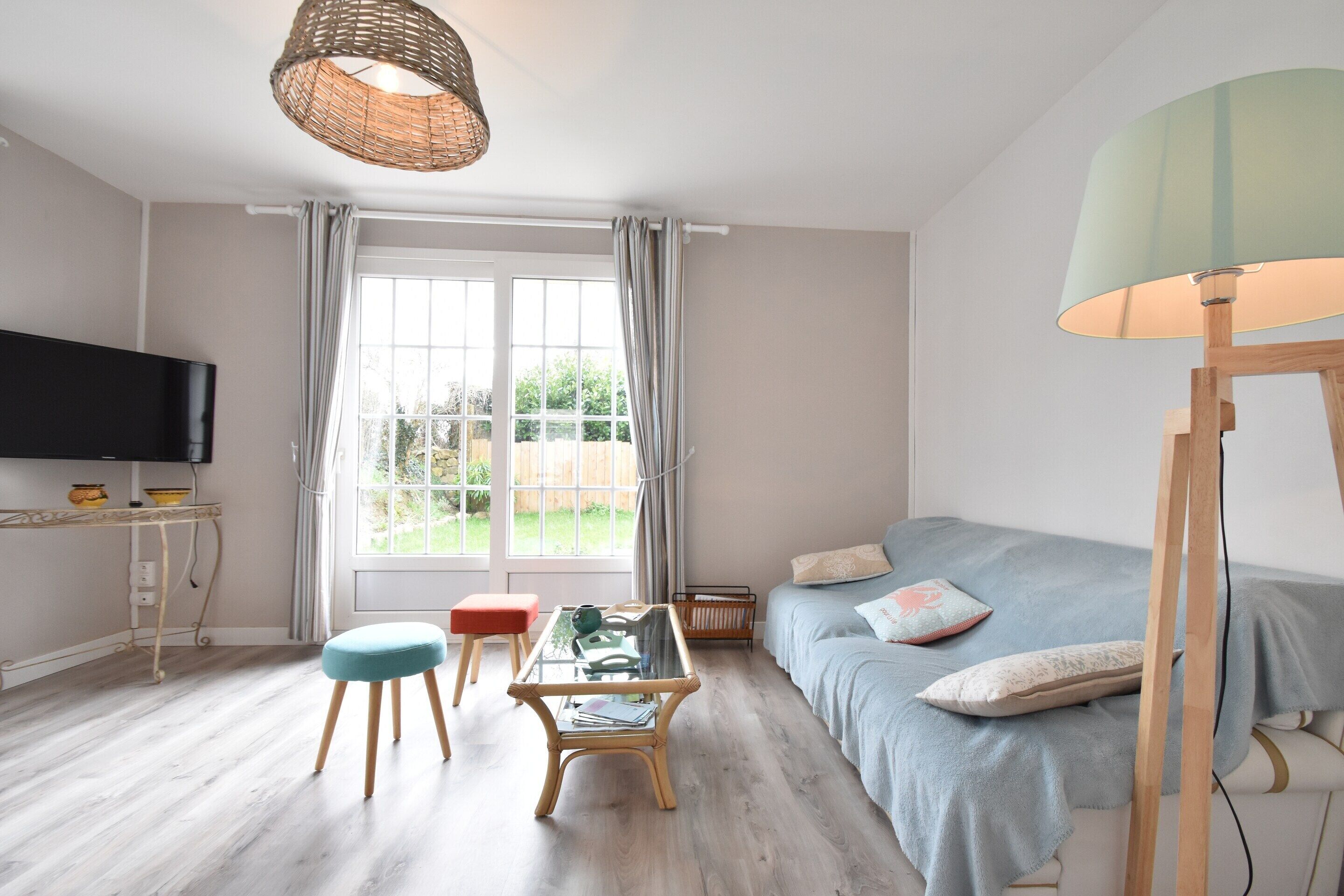 Ein Zimmer mit Fernseher, Sofa, Tisch und einem fensterbepflanzten Fenster.