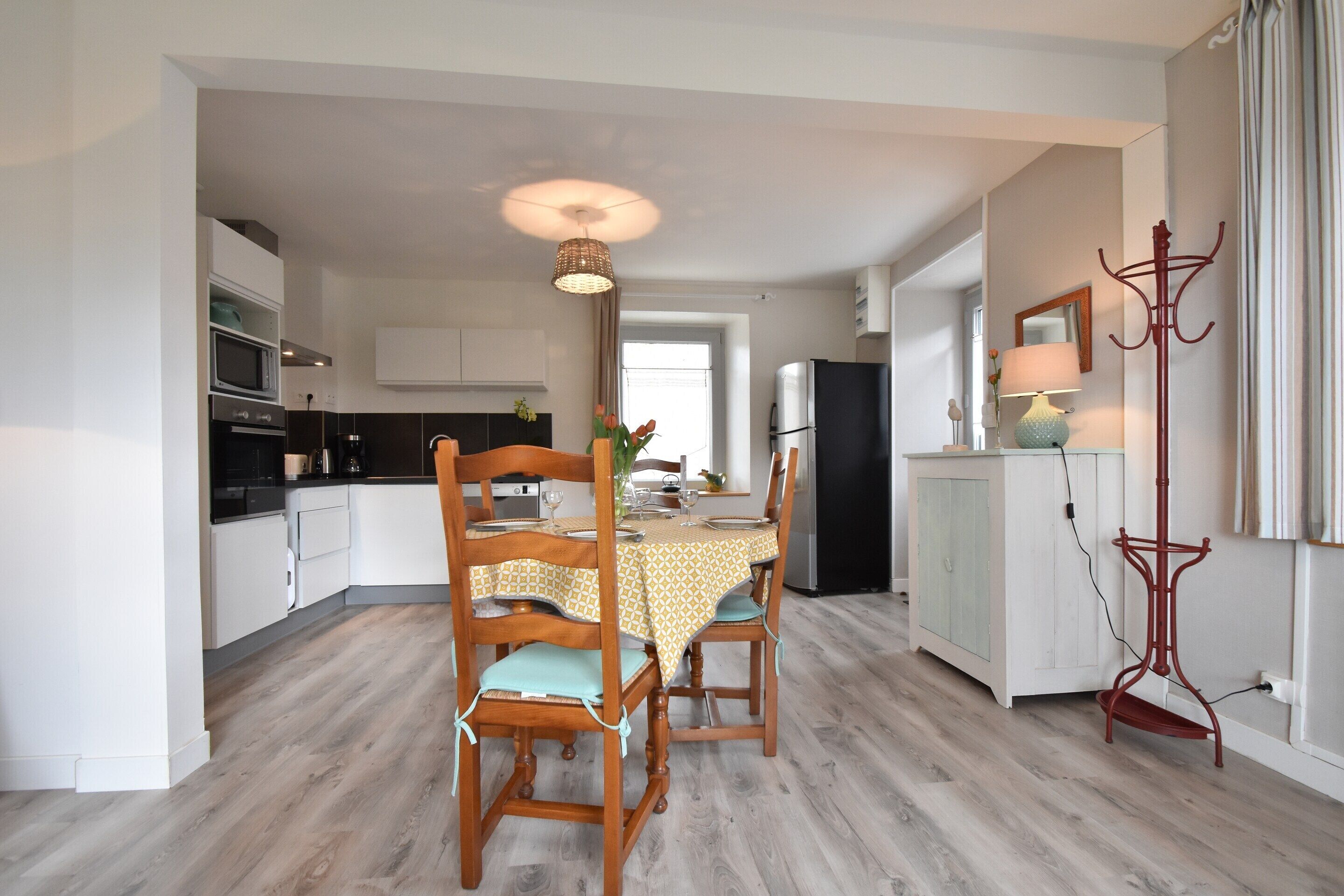 Een moderne keuken met witte kasten, een eettafel met stoelen, een hanglamp en een kapstok.