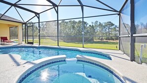 Une piscine dotée d’une enceinte en verre, d’un espace salon couvert et offrant une vue sur un paysage verdoyant.