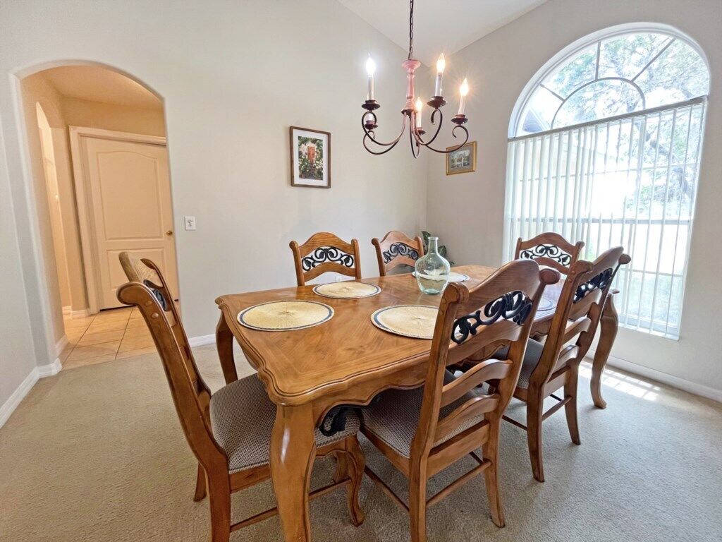 Comedor con mesa de madera y seis sillas, candelabro y ventana grande con vista a árboles.