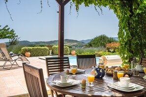Une table à manger avec des aliments pour le petit-déjeuner, une piscine et une vue sur le paysage.