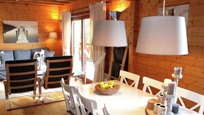 A wooden cabin interior with a dining table, chairs, a bowl of fruit, and a painting on the wall. - Poolside Bliss Near Lake (Beaulieu)