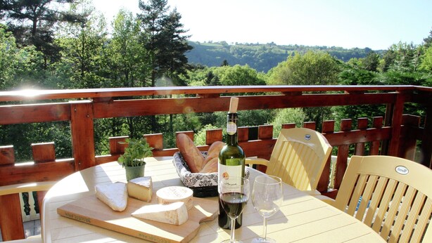 A table with a bottle of wine, glasses, cheese, and bread on a deck with a view of a forested landscape. - Poolside Bliss Near Lake (Beaulieu)