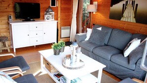 A cozy cabin interior with a grey sofa, white entertainment unit, and a painting of a pier. - Poolside Bliss Near Lake (Beaulieu)