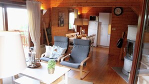 A cozy cabin interior with a dining area, two armchairs, a table with a lamp, a refrigerator, and a fireplace. - Poolside Bliss Near Lake (Beaulieu)