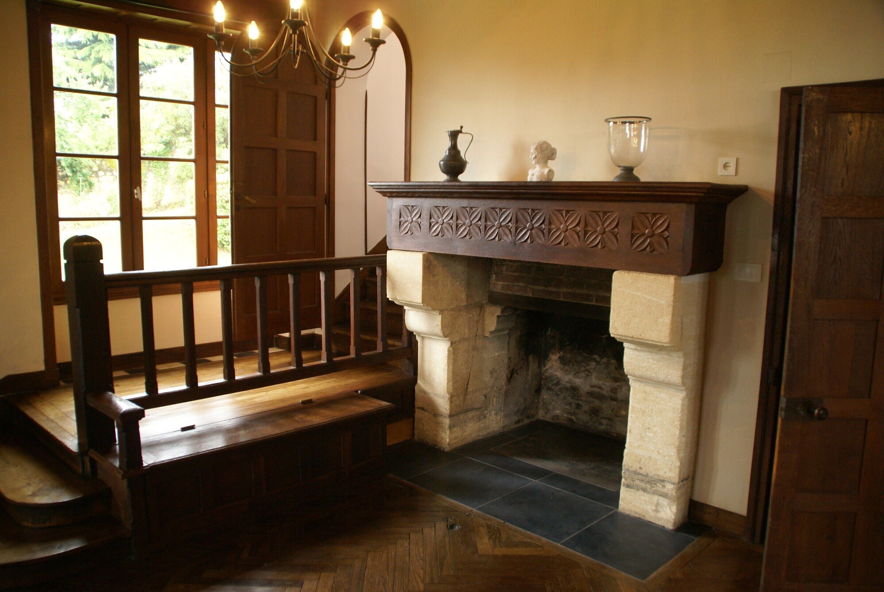 A room with a wooden bench, a fireplace with a decorative mantel, and a large window with multiple panes.