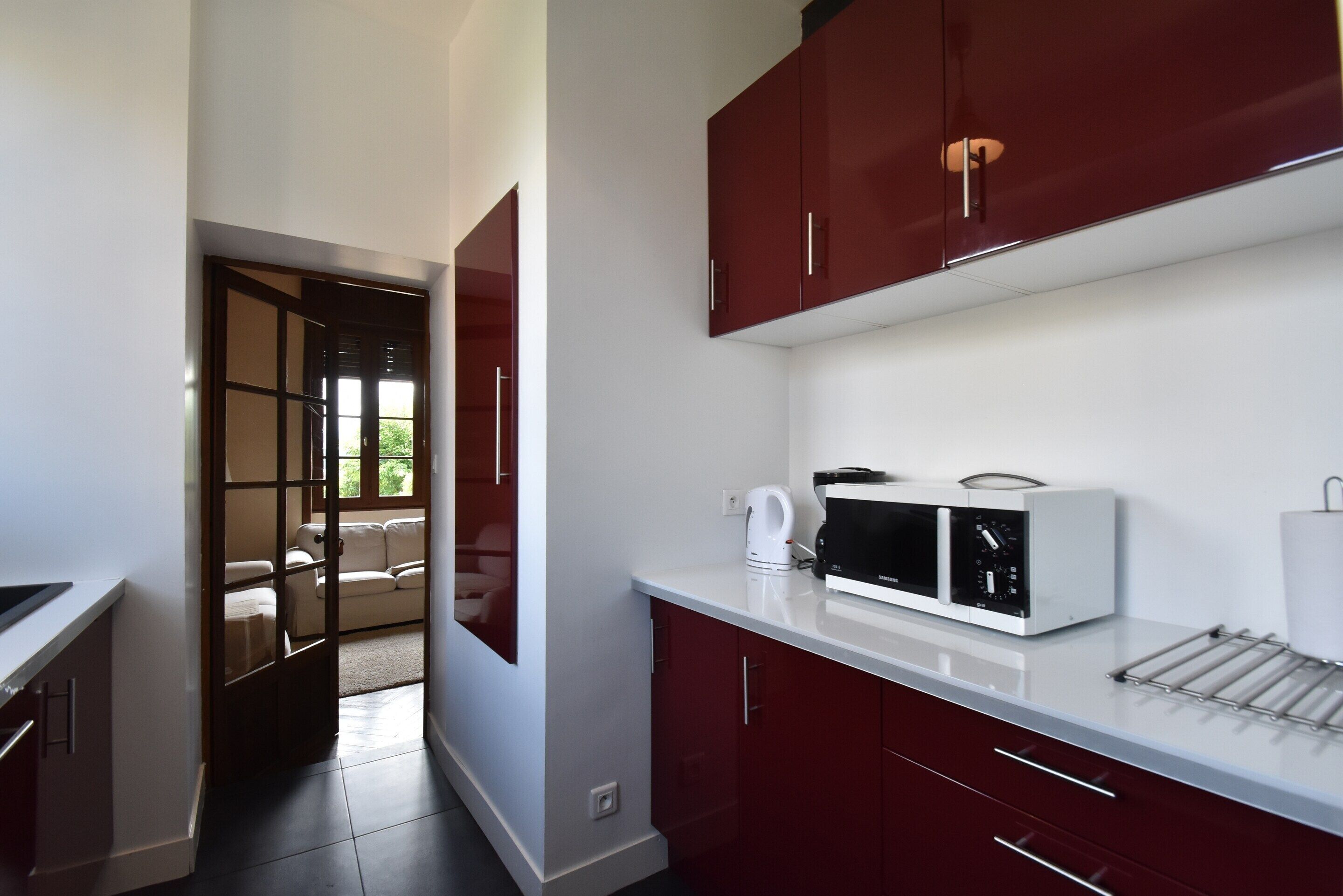 A modern kitchen with red cabinets, a microwave, and a kettle.