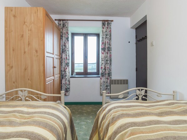 A bedroom with two beds, a window with floral curtains, a wooden wardrobe, and a radiator. - Normandy Countryside Stay (Gavray-sur-Sienne)